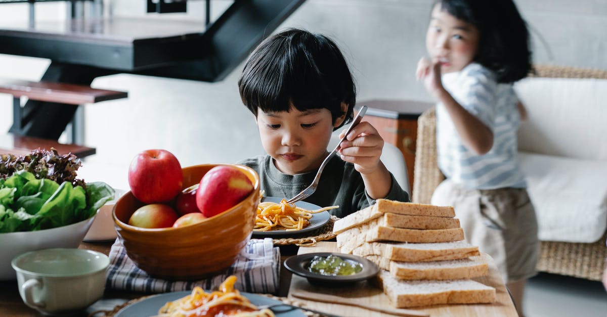 My pasta keeps sticking together - Active little Asian girl running behind brother having lunch in kitchen