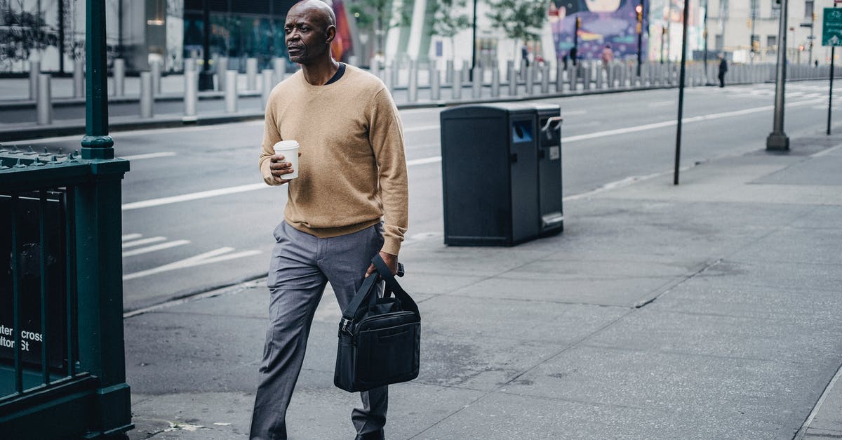 My sourdough starter is going wrong in every possible way - Full body of pensive African American male walking on pavement near asphalt road with takeaway coffee and black handbag in hand