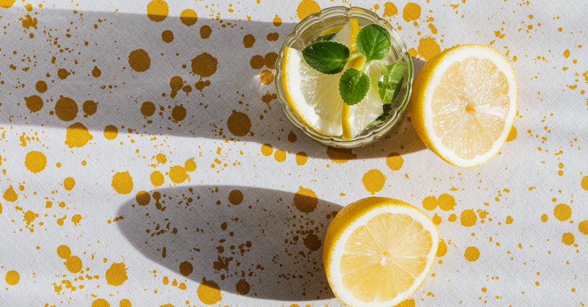 Mysterious bitter taste from tropical fruits and coconut - Top view of glass of fresh cold drink with halves of lemon on table with white tablecloth in yellow blots