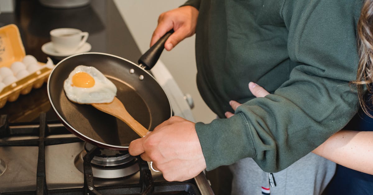 Need a gas cooker but have no gas supply - Crop anonymous female embarrassing man in casual clothes standing near gas stove with pan in hand and cooking fried egg for diner in kitchen at home