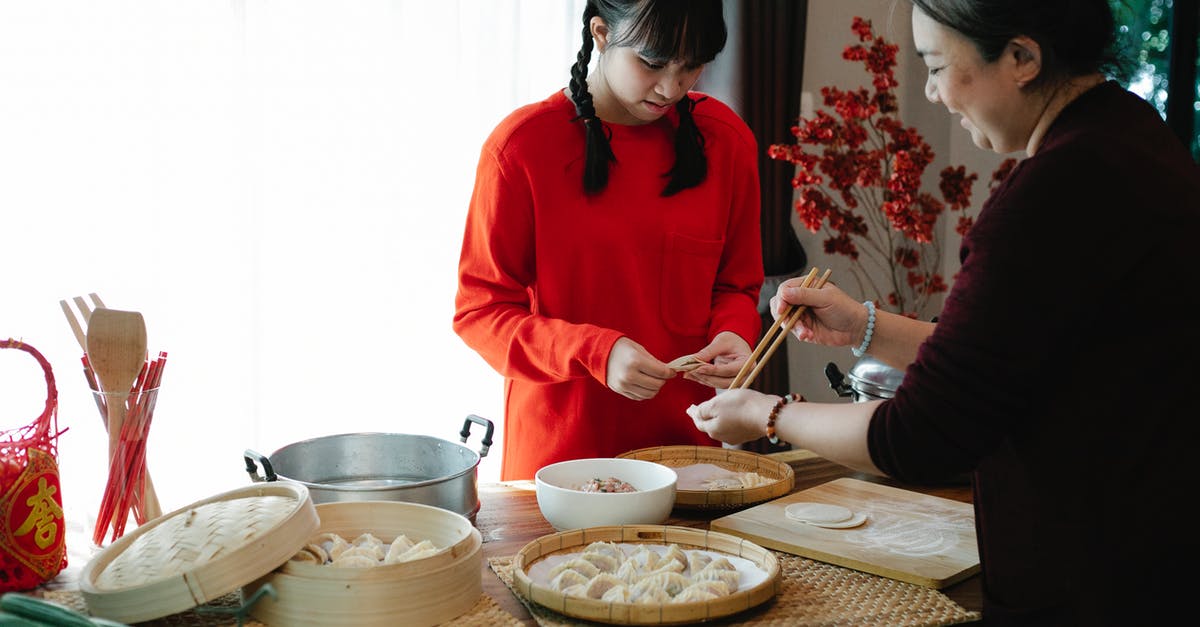 New to grinding meat - Cheerful ethnic grandma with attentive teen preparing dumplings at table with traditional steamers during New Year holiday at home