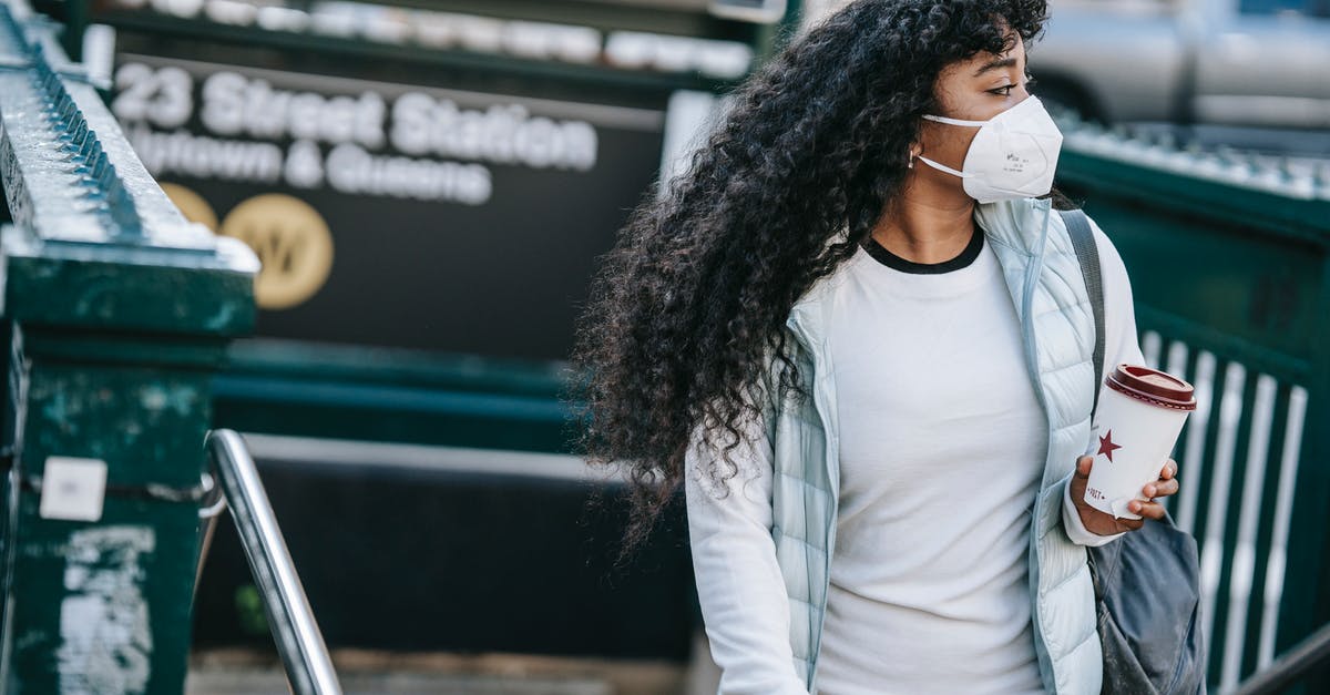 Normal coffee vs decaf - Emotionless African American female with coffee to go wearing casual wear and protective face mask leaving underground station and looking away in New York City