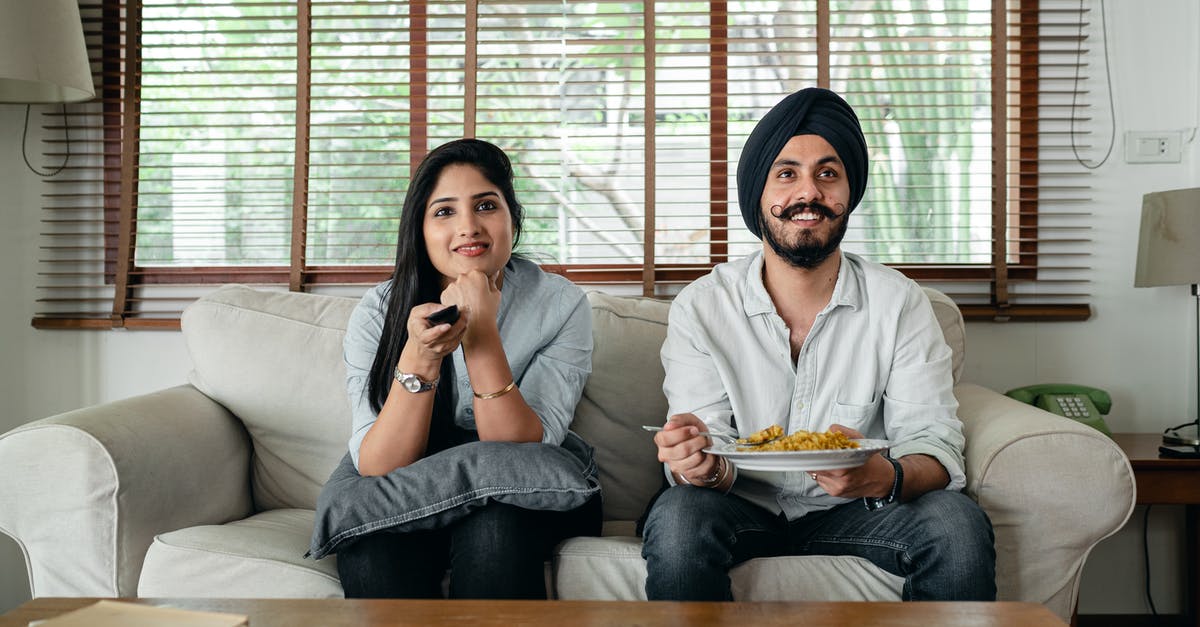 Nuke TV Dinner and then renuke it 3 hours later? - Positive male with plate of food and female in casual clothes sitting on sofa in living room and watching TV at home