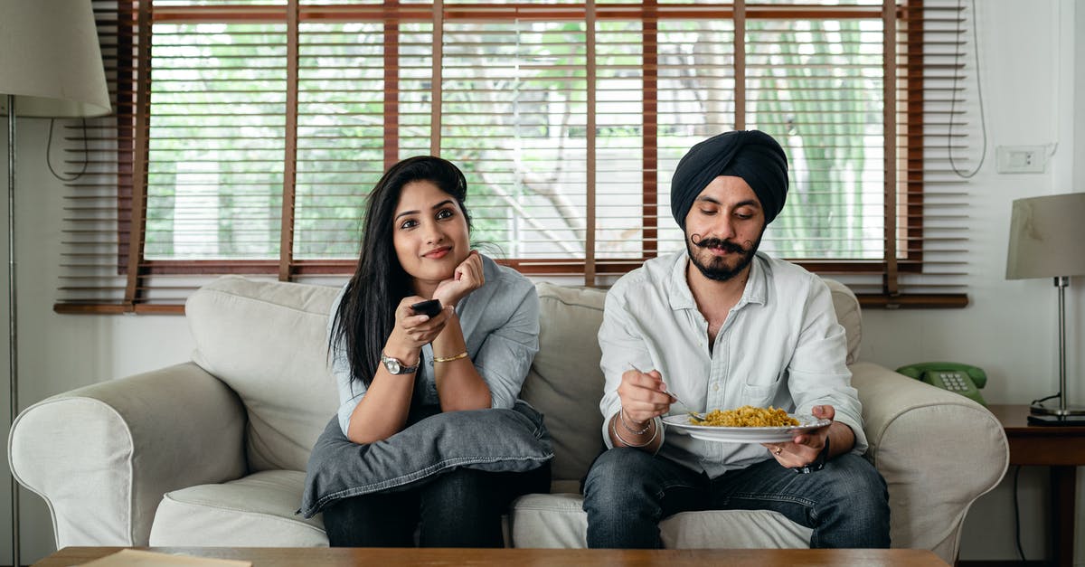 Nuke TV Dinner and then renuke it 3 hours later? - Pensive Indian male having meal on sofa while woman female in casual clothes sitting near and switching TV channels