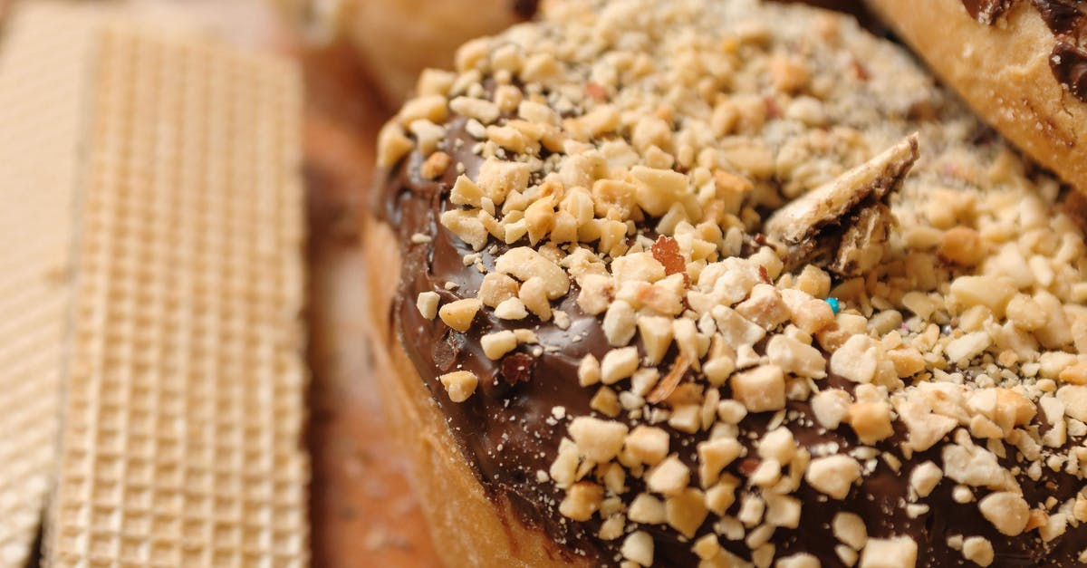 Nut/sunflower butter and cocoa - High angle sweet donut topped with chocolate frosting and chopped nuts placed near waffles on board