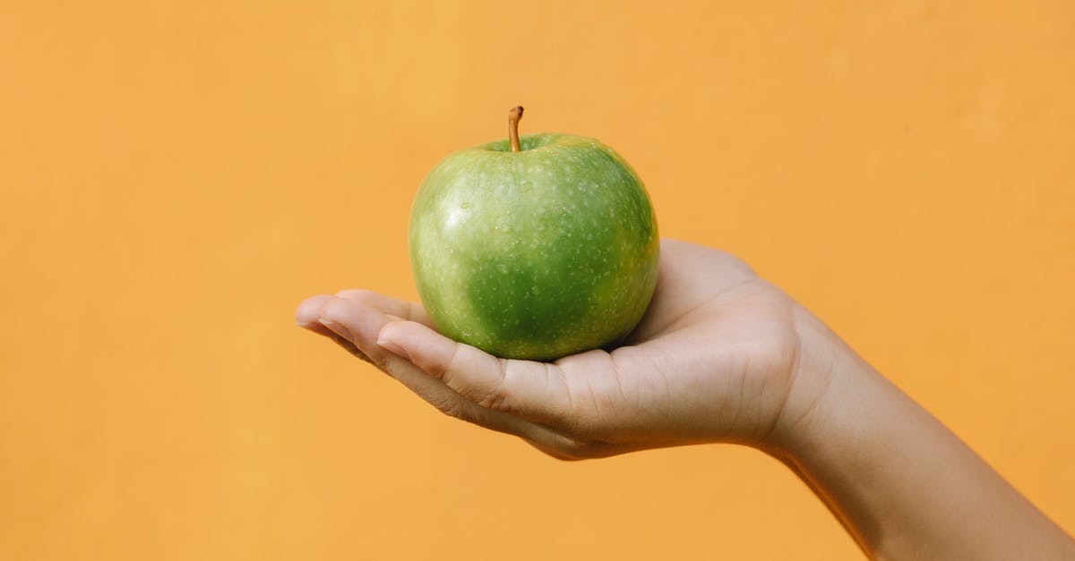 Oatmeal used in apple crisp topping - Crop anonymous female demonstrating fruit with thin green skin and crisp flesh against orange background
