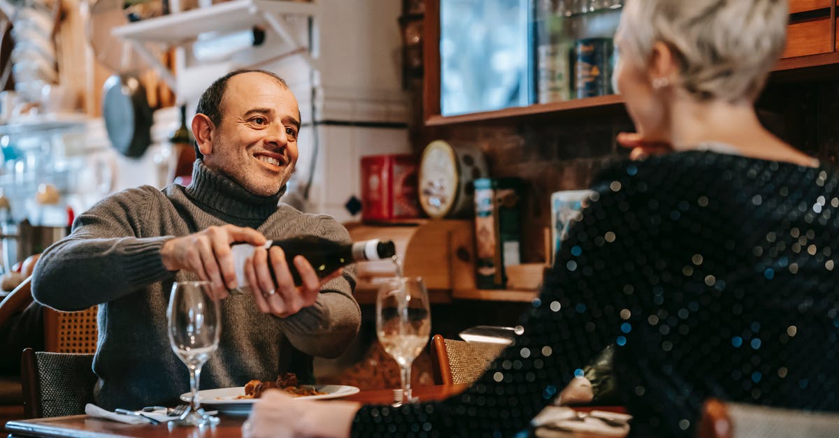 Opening wine bottle with rounded top using a waiter's friend - Positive couple having date at table while man pouring wine from bottle into wineglasses near plates with tasty dish in bright restaurant while looking at each other