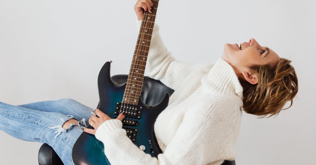 Oven does not have a temperature notification sound - Side view of cheerful short haired female in casual clothes laughing while playing electric guitar in comfortable armchair against white background