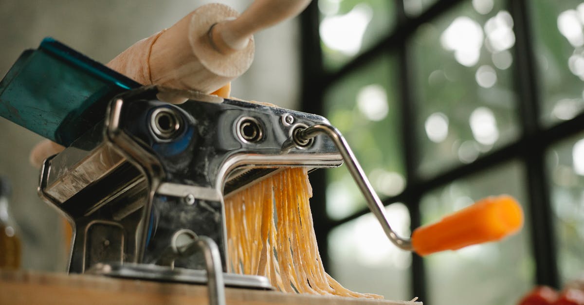 Pasta sticks to rolling cutters - From below of modern stainless pasta maker equipment with cut raw dough placed on wooden table in kitchen on blurred background