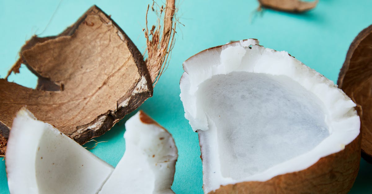 Peeling coconut meat from shell - From above of ripe coconut with soft white pulp and rough brown shell placed on blue background