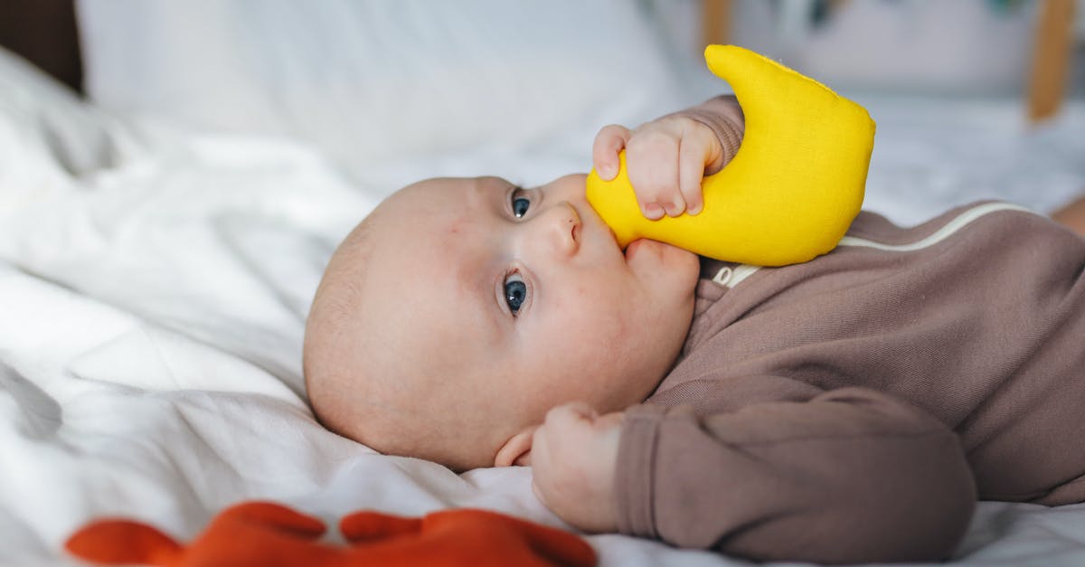 Peking Duck - why do they take my duck away? - Side view of adorable newborn in brown wear lying on bed with clenched fist and yellow toy in mouth