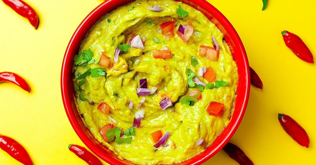 Pimento sauce that is added to mayo - Top view vivid composition of bowl with scrumptious fresh guacamole placed on yellow surface with red chili peppers arranged in rows