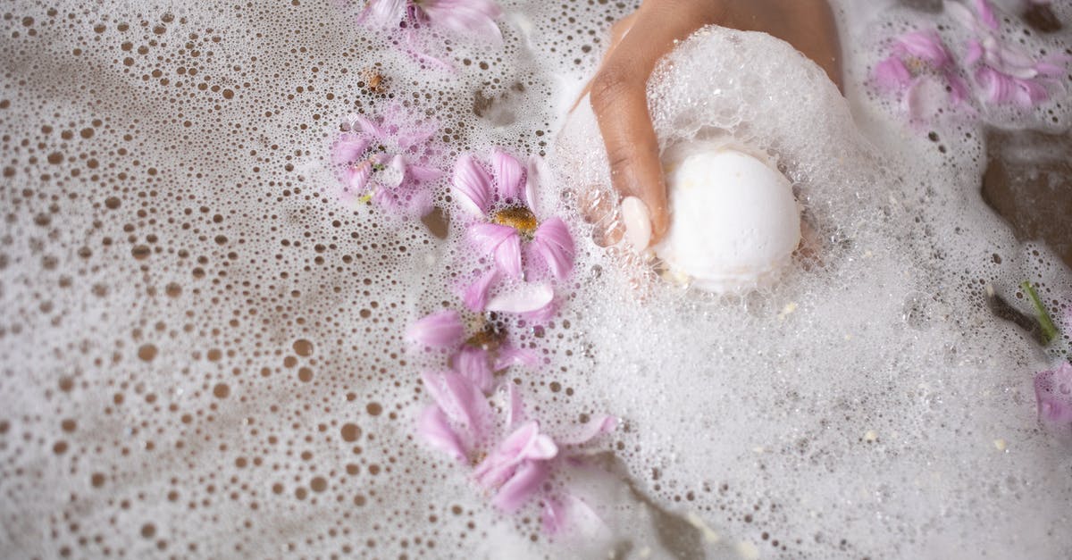 Pink salt vs regular salt - Woman holding ball of bath salt in water with foam and flowers