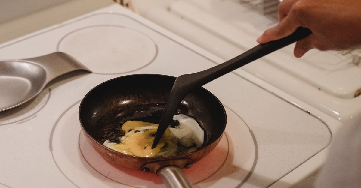 Place oil on cold or hot skillet? [duplicate] - Crop unrecognizable person near white stove with black spatula cooking scrambled eggs in kitchen