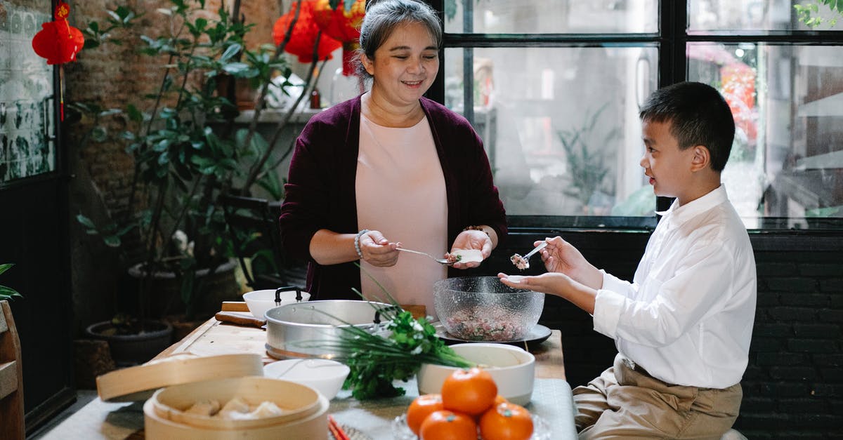 Please help identifying this herb - Side view of positive Asian preteen boy sitting at table in kitchen and helping smiling mature grandmother to prepare traditional Chinese dumplings for dinner