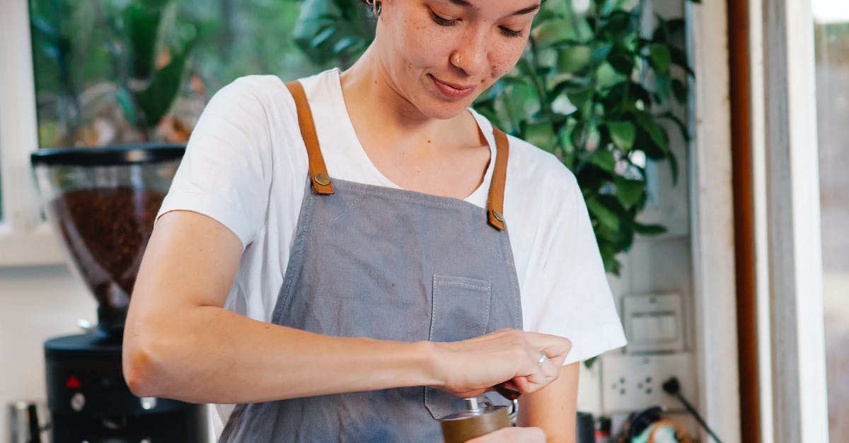 Please tell me what this kitchen tool is called and its use, specifically - Crop happy female in apron smiling and using grinder for preparing aromatic coffee in kitchen