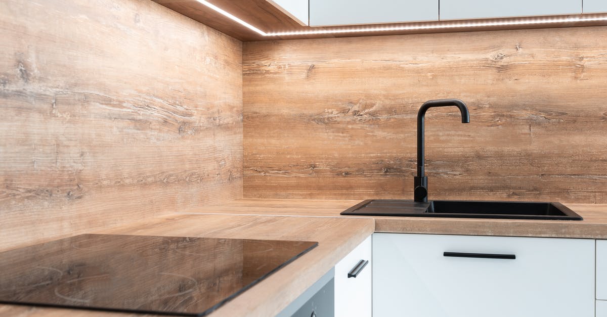 Popping corn on an electric stove - Modern black appliance and sink with faucet in stylish kitchen with wooden walls and white furniture