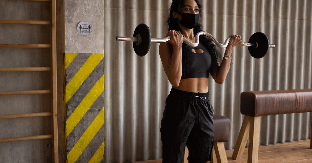 Pork belly strips and ribs - Black sportswoman in face mask exercising with barbell in gymnasium