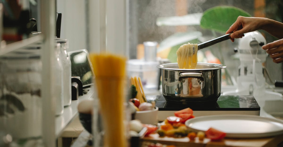 Preparing spaghetti without boiling water - Crop anonymous housewife picking freshly cooked Italian spaghetti from saucepan while cooking and serving food in light kitchen