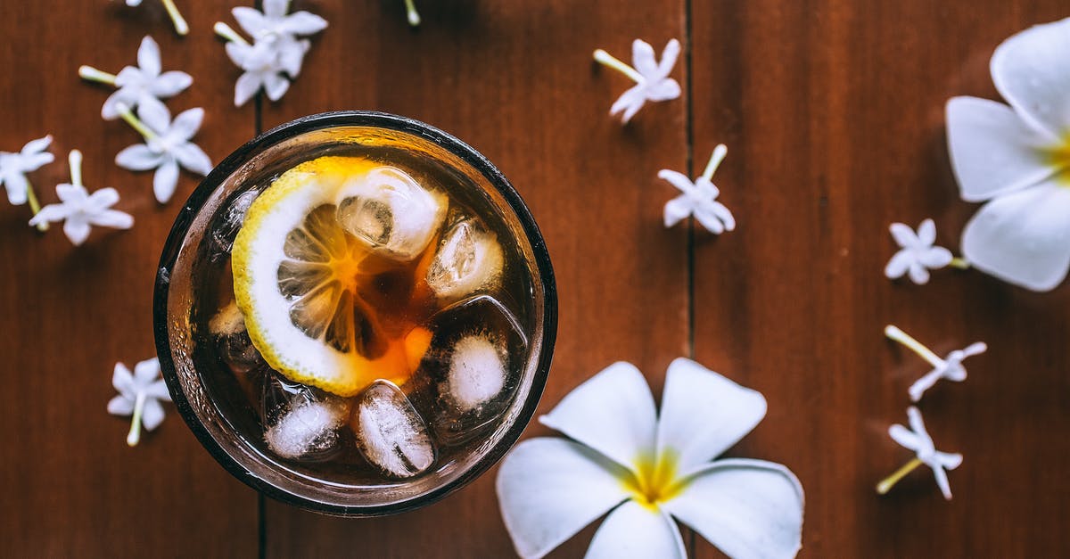 Preserved Lemons: is it ok if they are above the liquid - Top view of glass with fresh drink with slice of lemon and ice cubes on wooden background with plumeria flowers