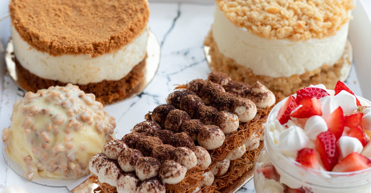 Preventing heavy top layer of cake from crushing cream layer - From above of set of tasty sweet deserts including tiramisu and round honey cakes near with glass jar of strawberry parfait served on white tray