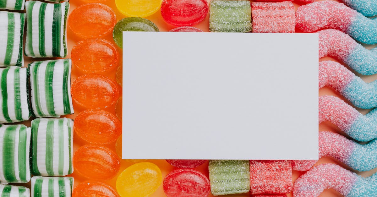 Preventing white sugar from clumping in the canister - Top view closeup of blank paper card placed on multicolored various shapes yummy candies in light confectionery