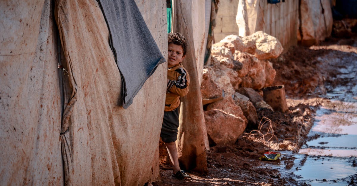 Problem Rolling Out Rough Puff Pastry - Little poor boy in muddy clothes looking at camera among old shabby brick houses with dirty fabric