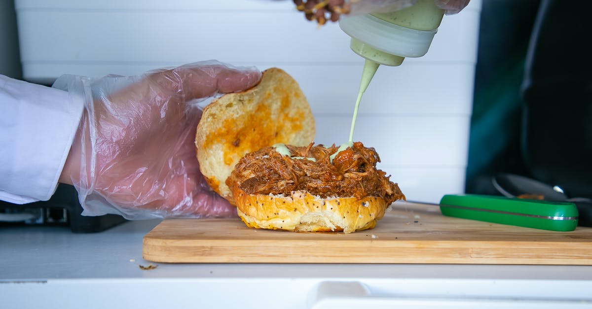 Pulled Pork for a large crowd - Crop anonymous male cook pouring mayonnaise sauce from bottle to fried pulled pork on bun in kitchen