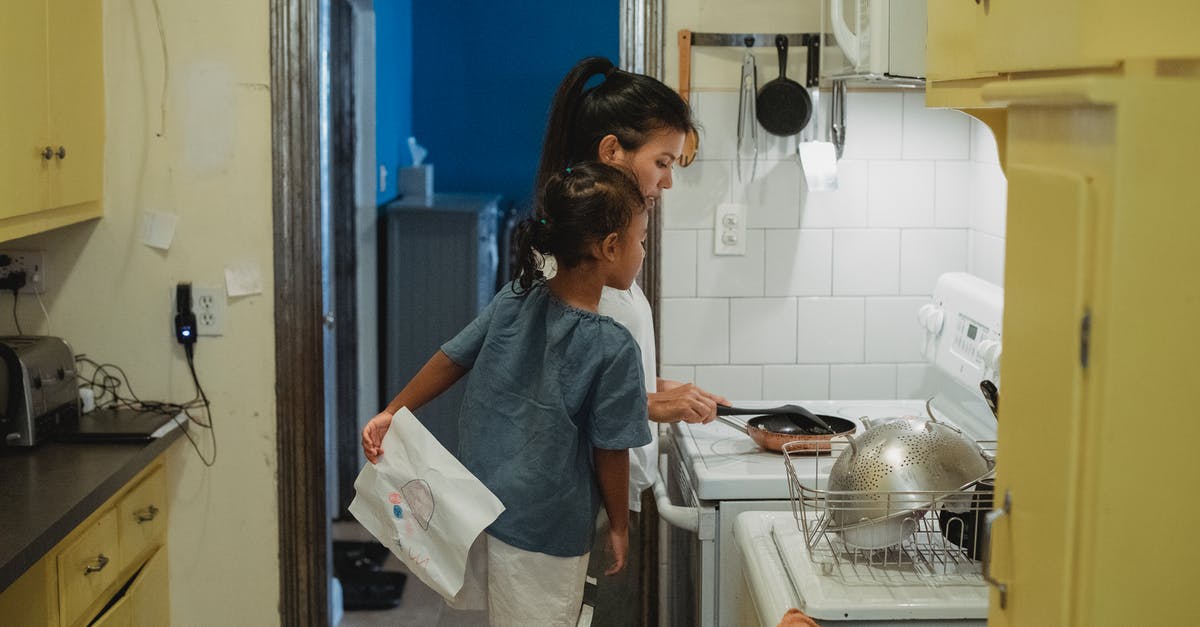 Putting a wet pan on hot stove top - Mother and daughter cooking in kitchen