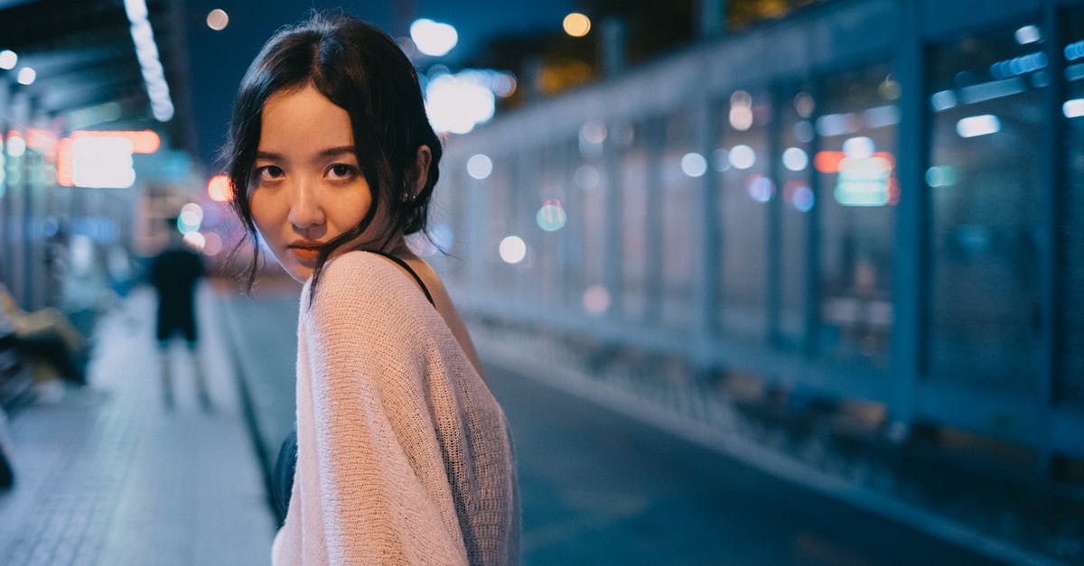 Quantity for over night oats - Content slim ethnic female looking over shoulder on blurred background of street with bright lights