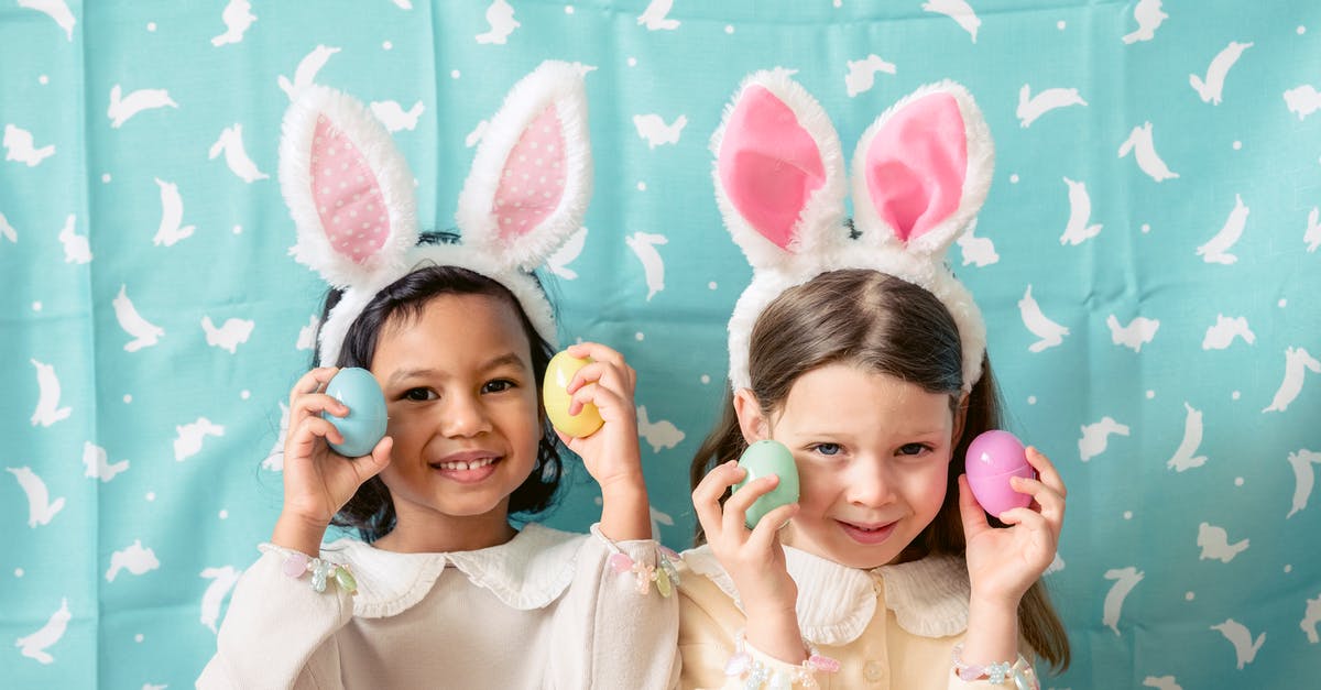 Rabbit that looks and tastes like chicken? - Content diverse children in hairbands with bunny ears showing decorative eggs while looking at camera against fabric with rabbit ornament