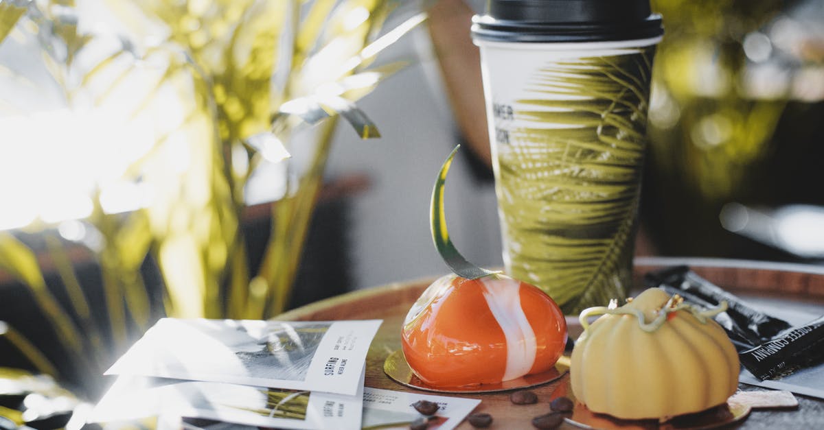 Recreating Tonka Bean Gu Cake - Delicious glazed mousse cakes with shiny and velvet surfaces decorated with colored chocolate near plastic glass of refreshment drink and spilled coffee beans on wooden table