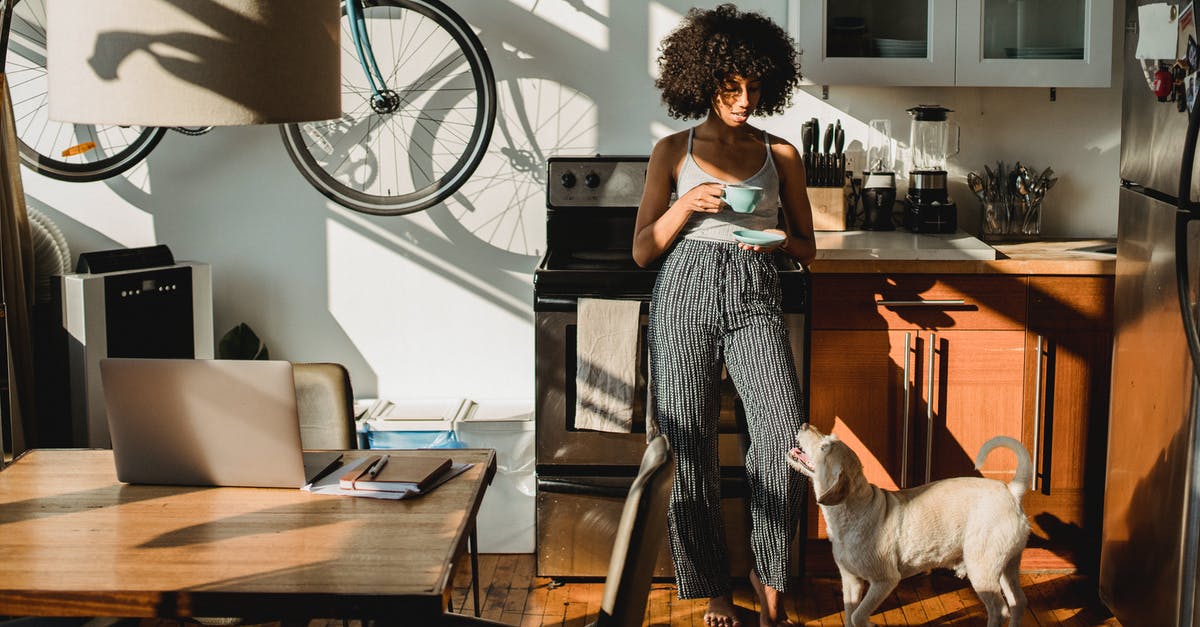 Refrigerate after opening, but why? - Young barefoot African American female with cup of hot drink standing on floor with dog at home