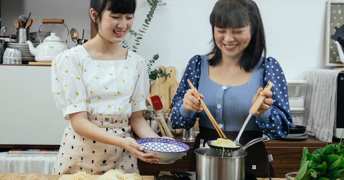 Reheating no boil lentil lasagna noodles after freezing - Happy Asian females in stylish clothes and aprons putting tasty boiled noodles into bowl while cooking traditional Asian dishes together in modern kitchen