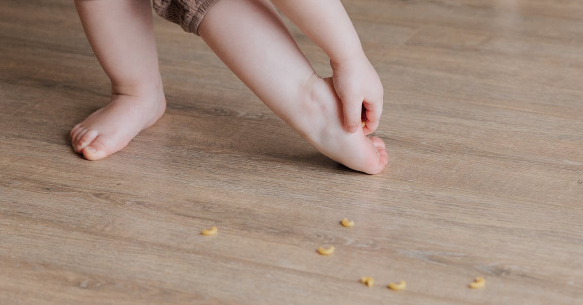 removing breast before roasting rest of duck? - Crop faceless toddler standing barefoot on floor and trying to remove stuck pasta from foot while playing and developing fine motor skills at home