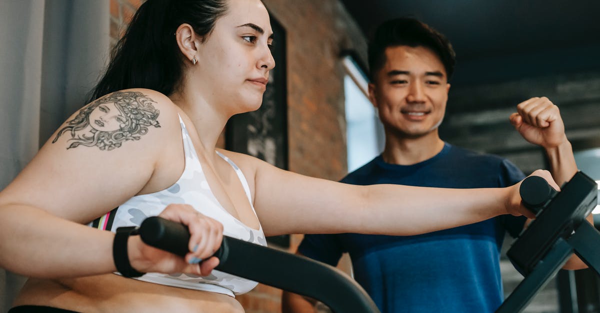 Removing fat from a recipe - From below of happy young Asian male trainer motivating exhausted young female client to to cardio fat burning exercise on elliptical machine in modern sport club