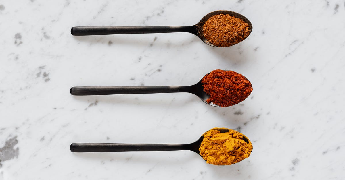 Removing turmeric colour from mortar and pestle - Top view of dry curcuma with smoked paprika and mix of ground peppers on plastic spoons on marble table