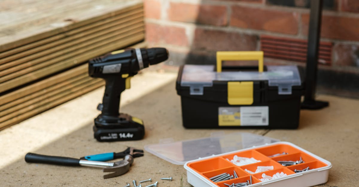 Restore Luster Craft - Electric screwdriver on floor near containers with instruments placed near spanner with hammer against brick wall  and wooden barrier