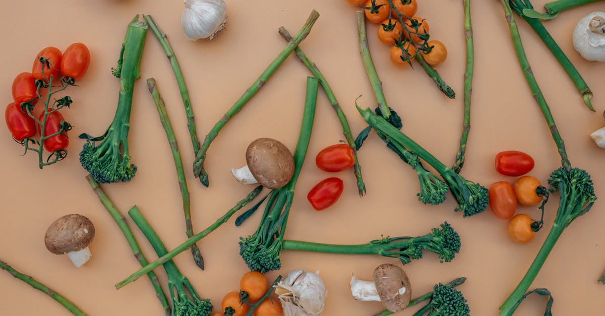 roasted garlic vs. raw - Top view of healthy raw cherry tomatoes with mushrooms and garlic arranged on beige table with fresh asparagus and broccoli