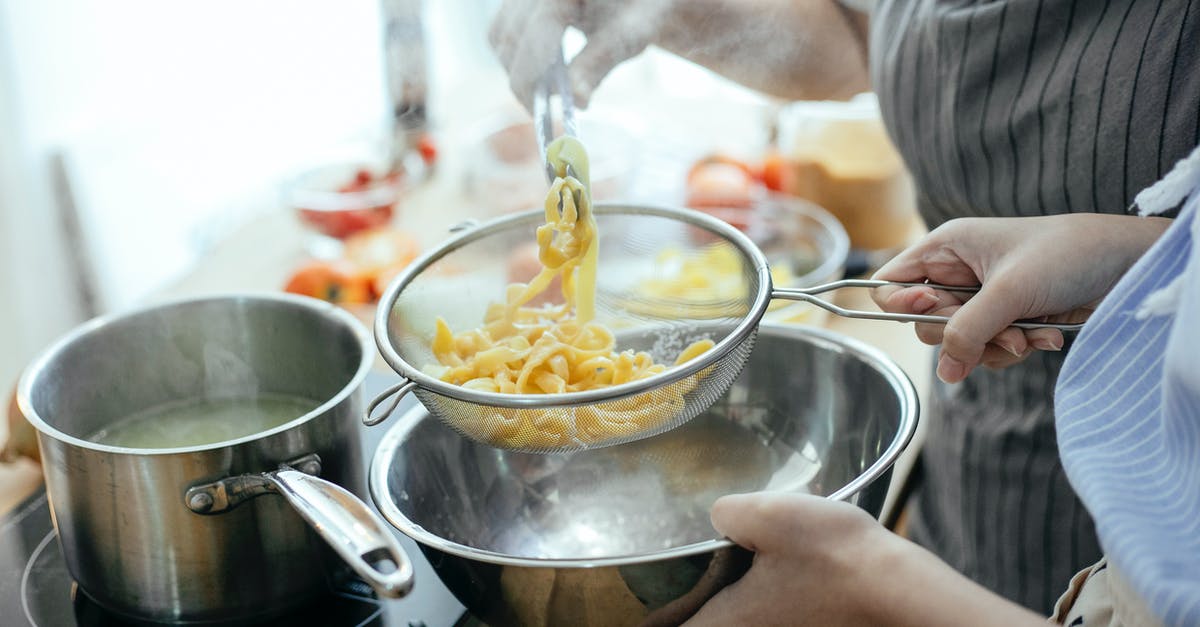 Rolling boil has barely any steam? - High angle of crop faceless female chefs putting noodles from saucepan with boiling water into strainer while standing at table with ingredients in kitchen