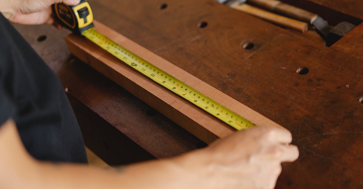 Royal icing - how important is accurate measuring? - Unrecognizable male carpenter standing at wooden workbench and measuring length of board with yellow tape measure while working in professional studio