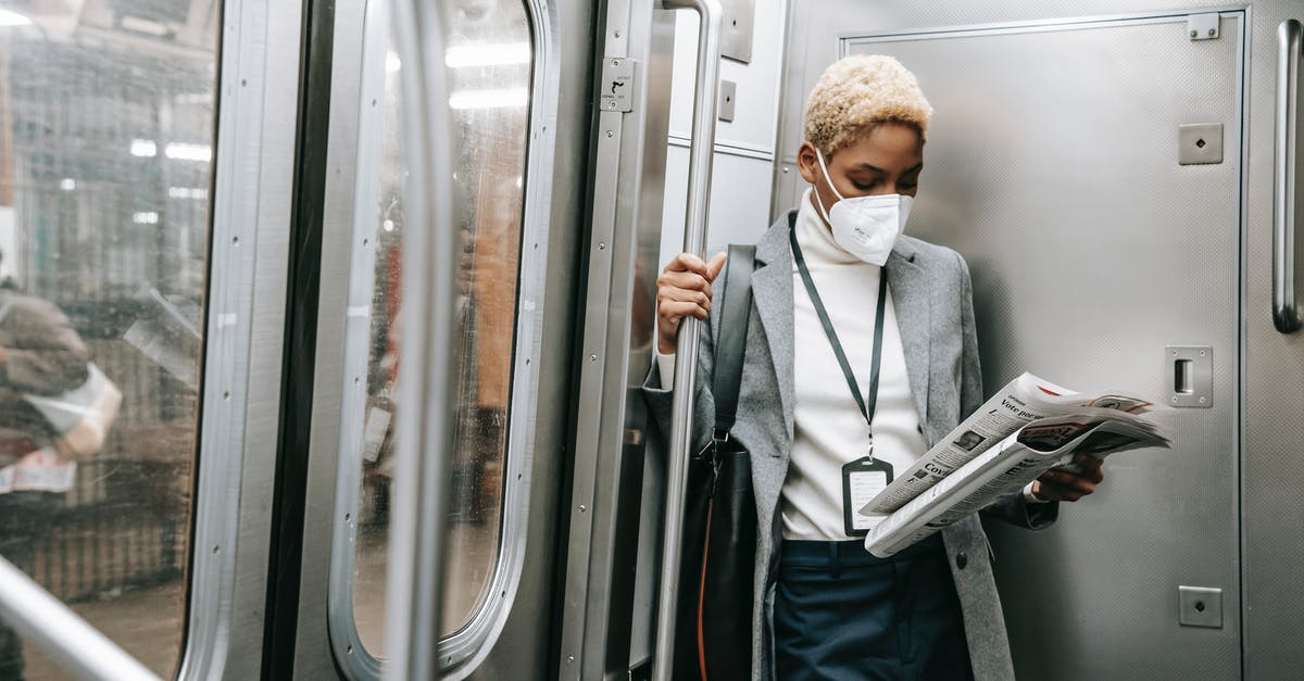 Royal icing safety concern - Concentrated young African American female in formal outfit and protective mask reading fresh newspaper while standing in metro train corner