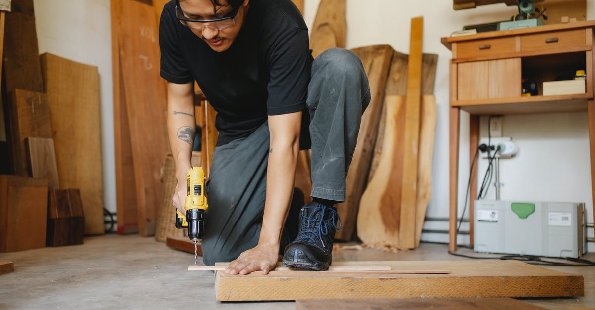 Safety glasses in the kitchen: why are these not common place? - Ethnic man leaning on wooden plank and drilling hole