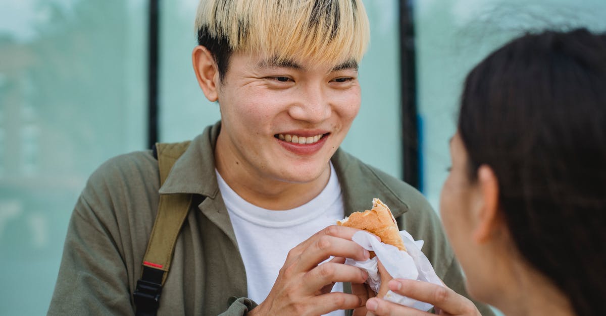 Sausage exploded and looks foamy - Crop woman hand feeding cheerful Asian boyfriend with hot dog