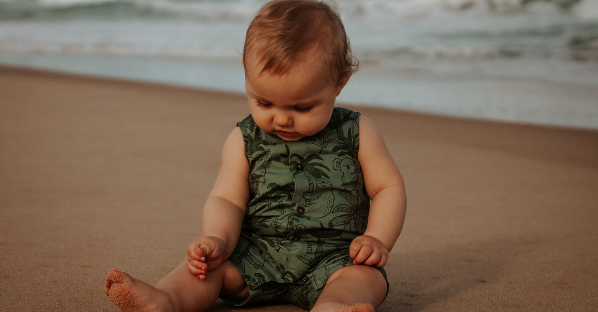 Sausage exploded and looks foamy - Cute baby in ornamental wear resting on sandy sea shore