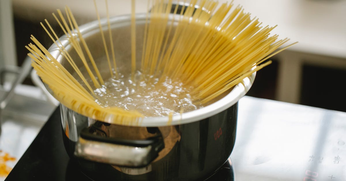 Saving pasta water - Raw spaghetti cooked in boiling water in saucepan placed on stove in light kitchen