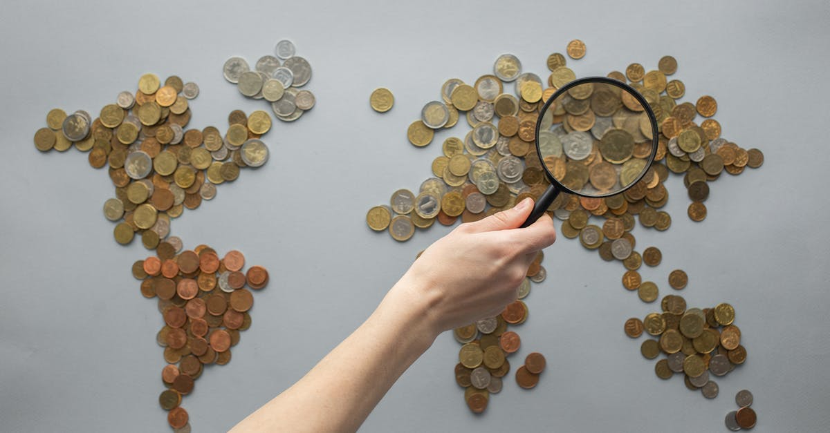 Search terms for potatoes inside of a bun - Top view of crop unrecognizable traveler with magnifying glass standing over world map made of various coins on gray background