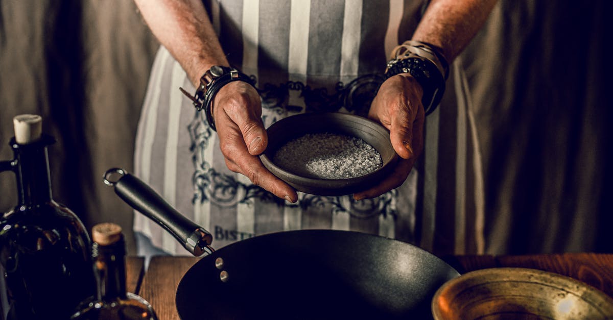 Seasoning on Magnalite anodized aluminum fry pans needs to be removed and re-done, what is process? - High angle of crop unrecognizable male chef adding kosher salt in pan while cooking traditional lunch in restaurant kitchen