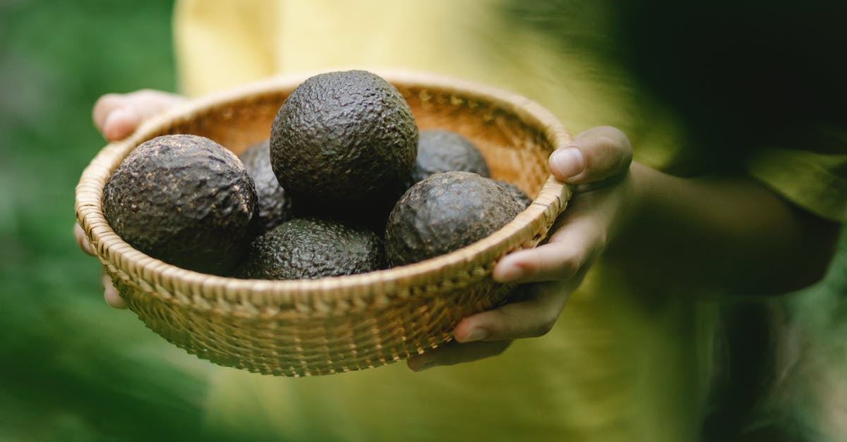 semi-freezing ripe avocado for easier handling - Crop faceless female holding wicker bowl full of avocado while standing in garden