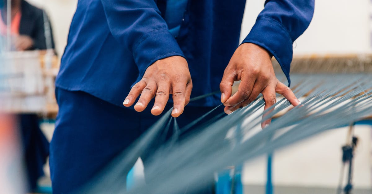 Separate coconut oil using microwave - Crop unrecognizable craftsman in blue uniform unraveling thin threads on loom machine while working in studio with ethnic colleague